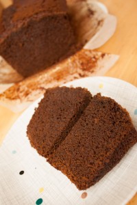 A slice of Jamaica Ginger Cake cut into two on a plate, with the cake in the background.
