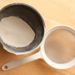 Bowl with sifted flour in it next to a sieve
