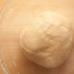 Bread dough for making Bath buns after the first rising. The dough is in a glass bowl covered with plastic wrap.