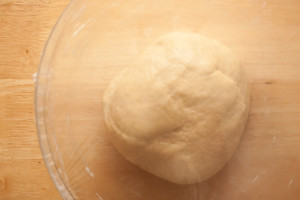 Bread dough for making Bath buns after the first rising. The dough is in a glass bowl covered with plastic wrap.