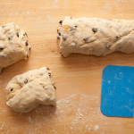 Yorkshire teacake dough on a lightly floured wooden surface. The dough has been cut into three pieces using a blue dough scraper.