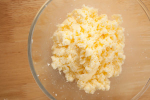Butter and sugar creamed together in a glass bowl on a wooden surface.