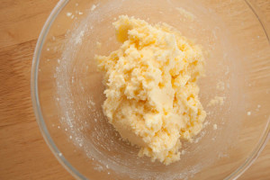 Creamed butter and sugar with egg mixed in. The mixture is in a glass bowl on a wooden surface.