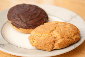 Two Grantham Gingerbread biscuits / cookies on a plate. One of the gingerbreads has been coated with dark chocolate on top.